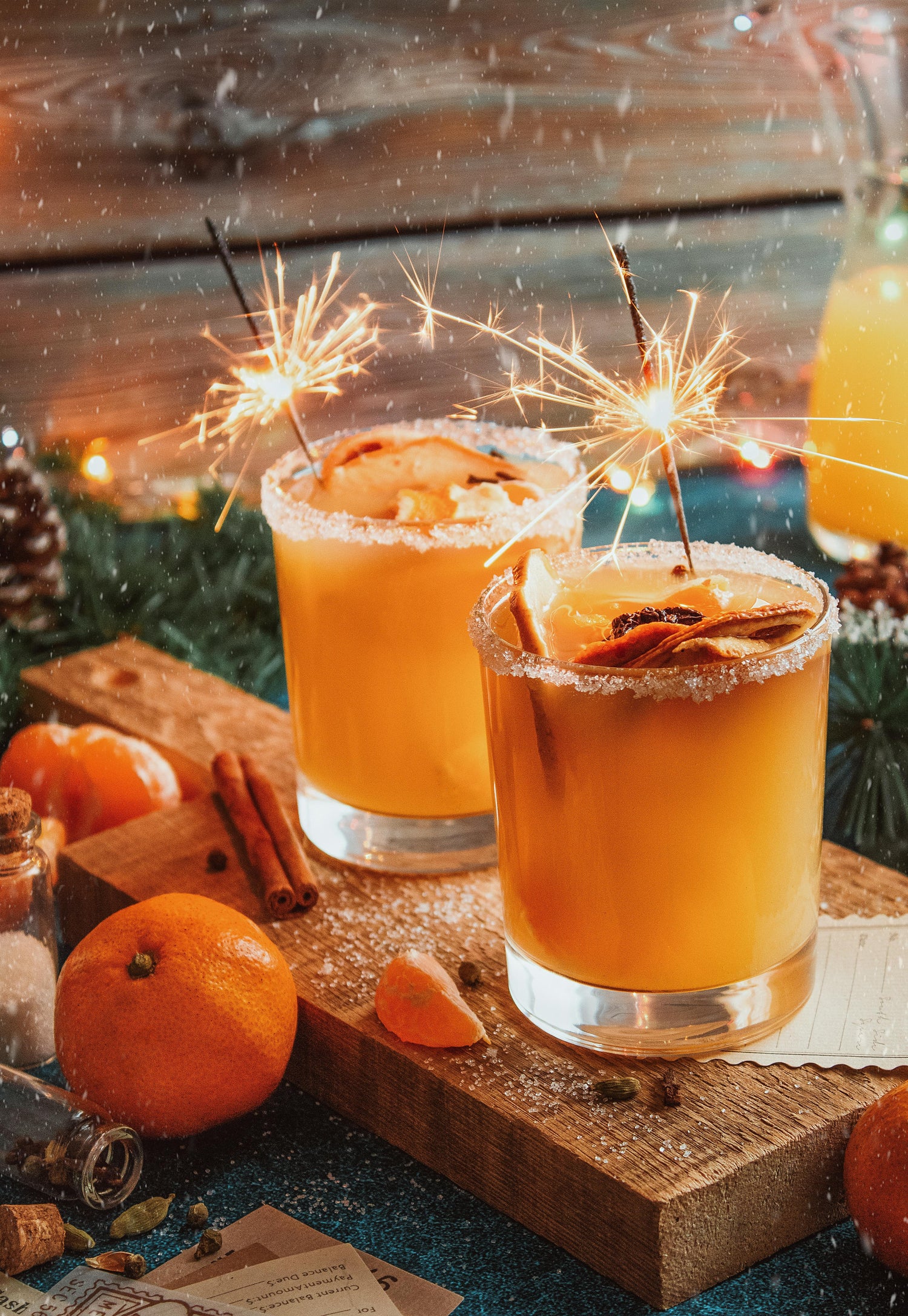 Two glasses of orange drinks with cinnamon sticks and sparklers on a wooden board.