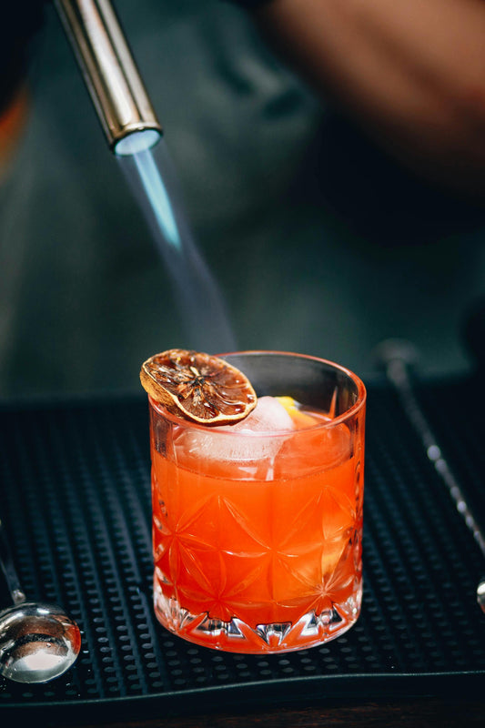 Cocktail being prepared with a blowtorch on a bar surface